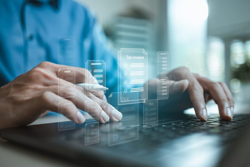 Osoba koristi laptop dok se na ekranu prikazuju digitalni dokumenti i fakture, simbol elektronskog poslovanja i digitalnog arhiviranja